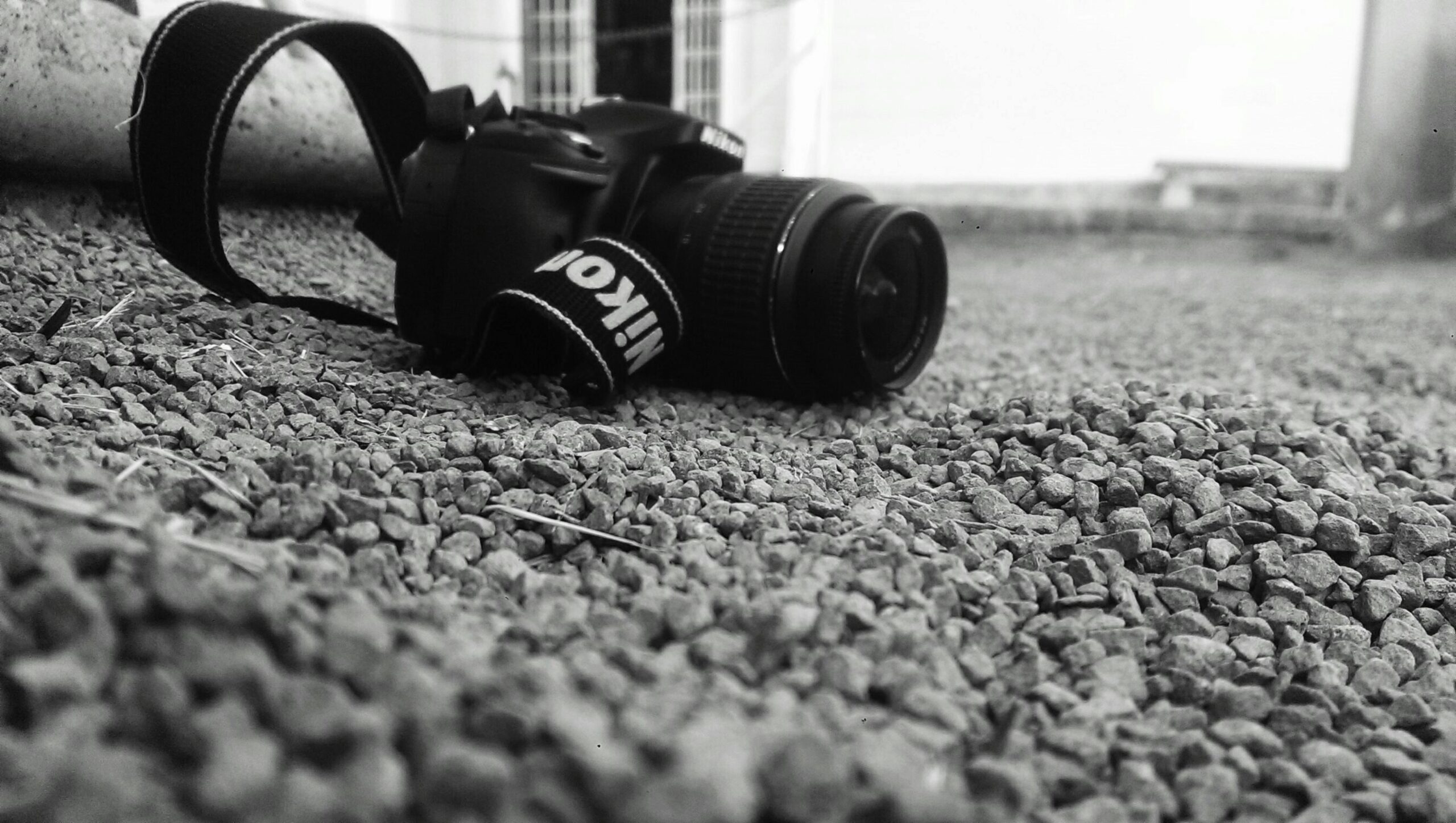 Close-up of DSLR camera on pebbled ground in black and white setting.
