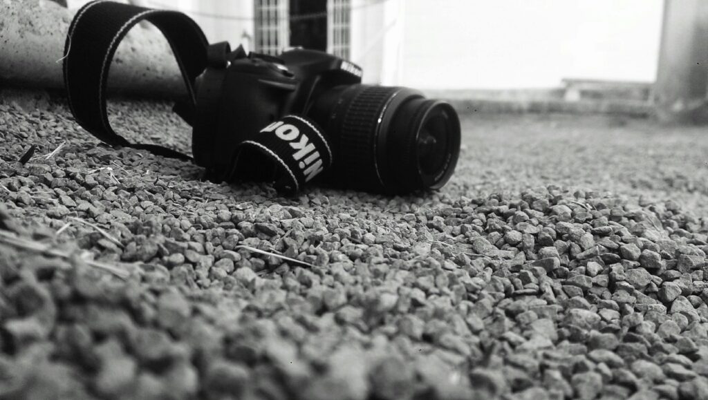 Close-up of DSLR camera on pebbled ground in black and white setting.