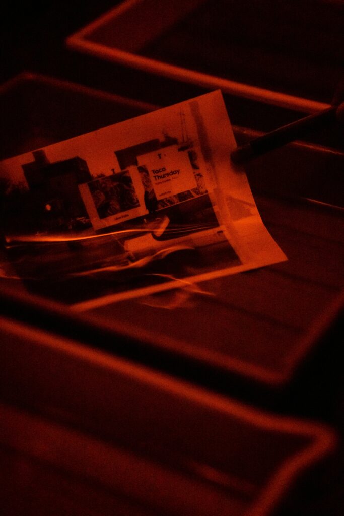 A photograph being developed in a darkroom with red lighting, highlighting traditional film processes.